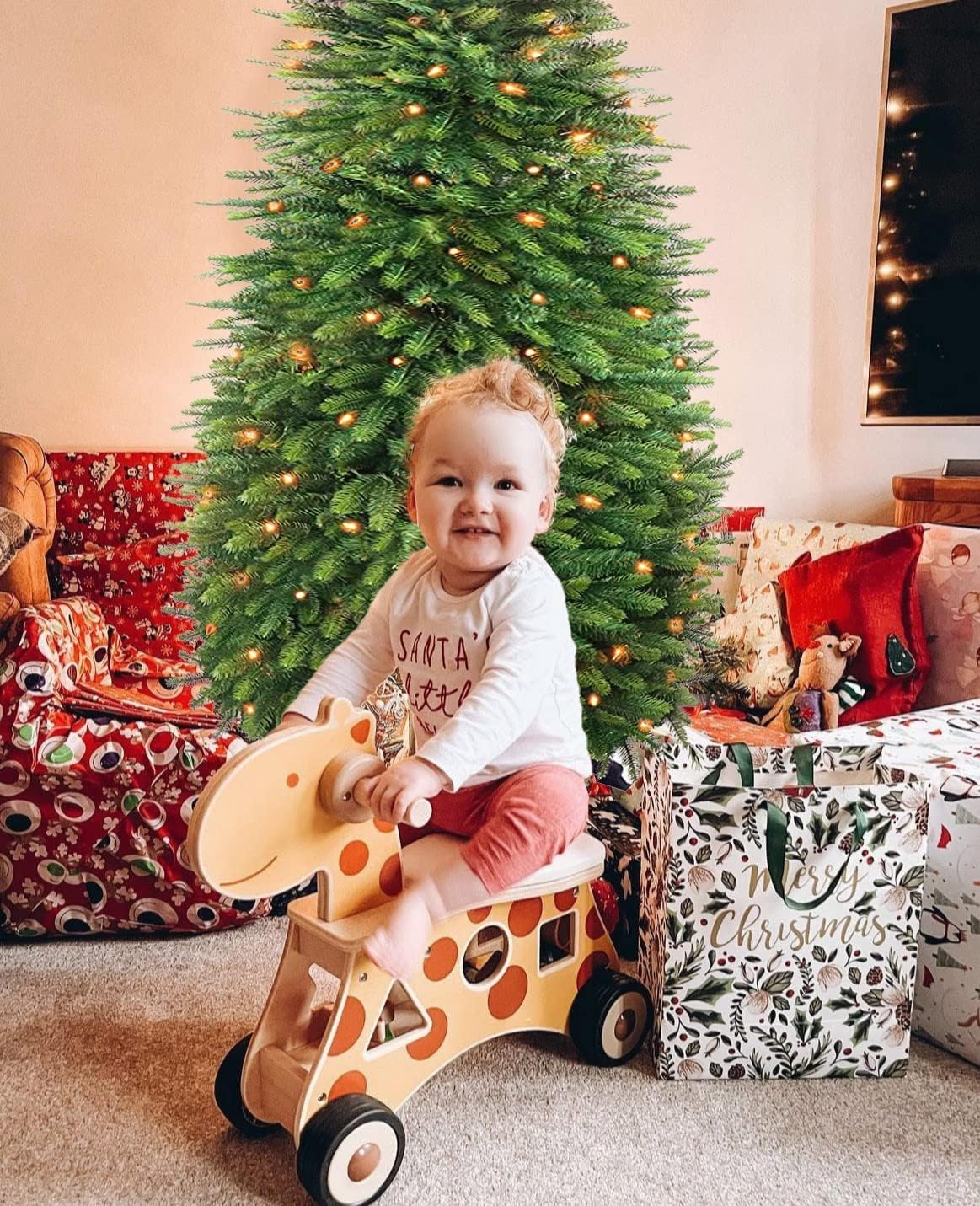 Child playing with a toy horse in front of a Fully assembled 6ft pre-lit pop-up Christmas tree glowing in a living room.