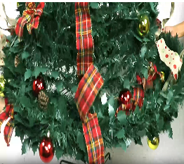 Expanding the decorated Christmas tree with red ornaments and plaid ribbons.